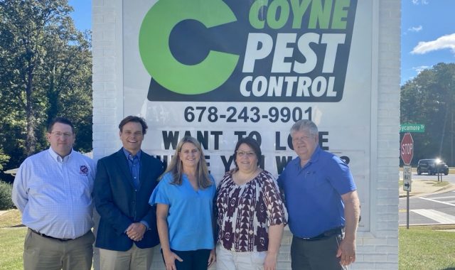 Representatives from Bug Busters and Coyne Pest Control standing in front of the Coyne Pest Control road sign